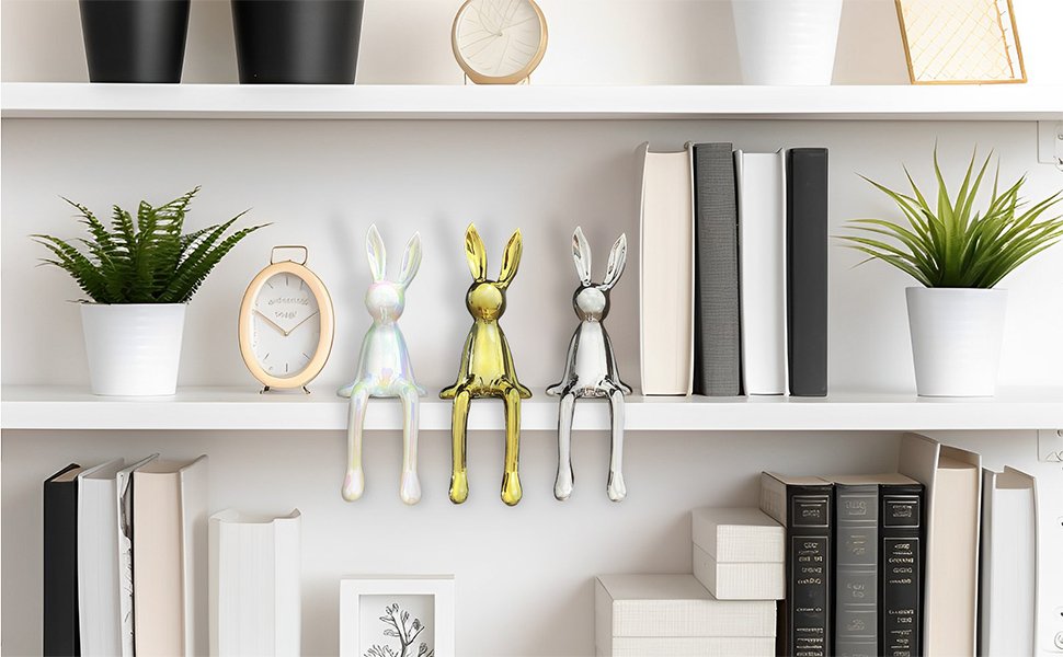 Three gold, silver and white bunny ornaments on a white bookshelf